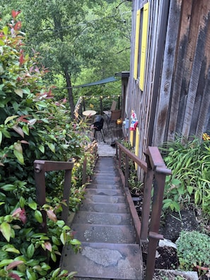 A wooden staircase leading to a building with a yellow door, surrounded by greenery. - Rustic, Artsy & Cozy Getaway Cabin in Laurel Highlands- minutes from Ligonier (Ligonier)