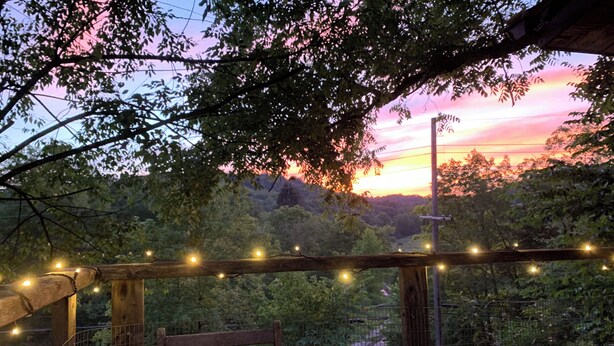 A wooden bench under a string of lights, surrounded by greenery and a sunset view. - Rustic, Artsy & Cozy Getaway Cabin in Laurel Highlands- minutes from Ligonier  (Ligonier)