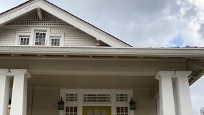 A house with a yellow front door, white columns, and a porch with steps leading to the entrance.
