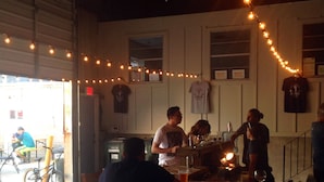 An indoor dining area with wooden tables and chairs, string lights, and a bar counter.