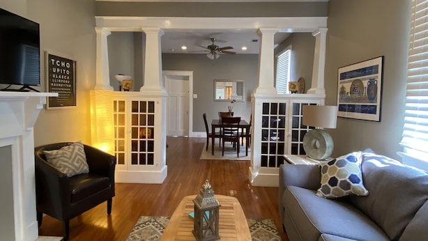A living room with a fireplace, a sofa, a coffee table, and a dining area in the background.