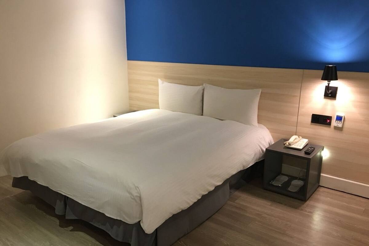 Habitació d'hotel amb un llit gran, una taula de nit amb un telèfon i una làmpada penjada a la paret.