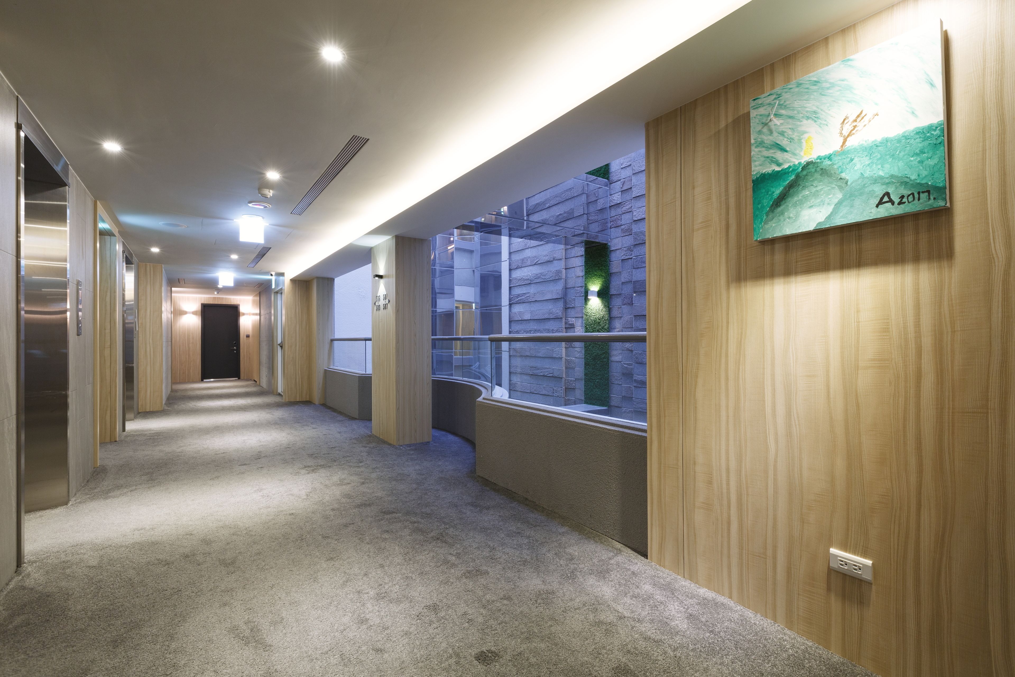 A hallway with carpeted floors, wooden walls, and a painting of a landscape.