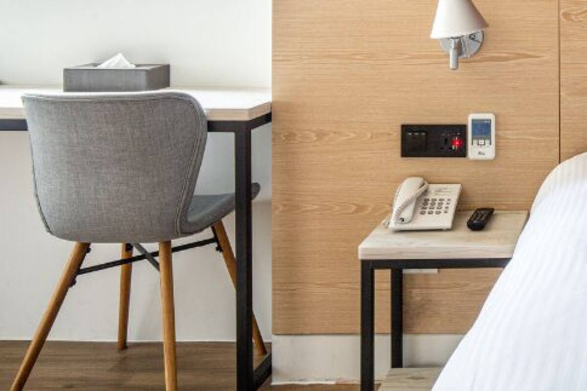 Habitació d'hotel amb un llit, un escriptori amb una cadira, una làmpada, un telèfon i un panell de control.