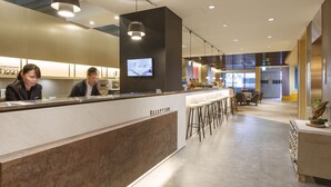 A modern reception area with a counter, bar stools, and a television screen. - Hub Hotel (Taoyuan City)