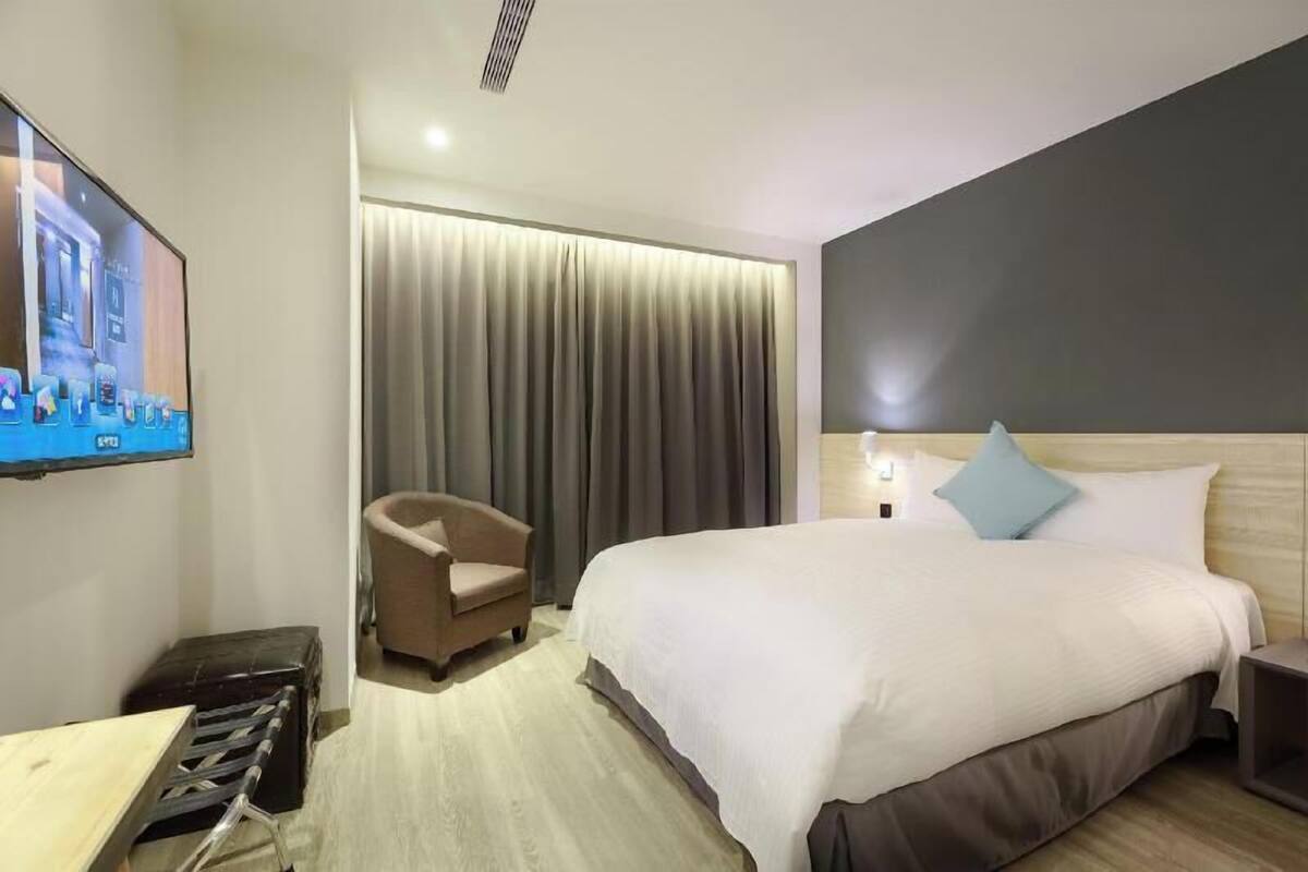 Habitació d'hotel amb un llit, televisió, una cadira i una cortina.