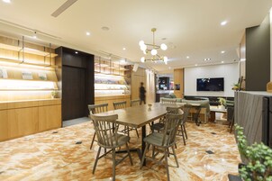 A modern dining area with a wooden table and chairs, a counter with informational displays, and a television mounted on the wall.
