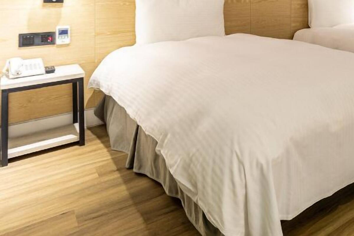 Habitació d'hotel amb dos llits, una taula de treball, una cadira i un paviment de fusta.