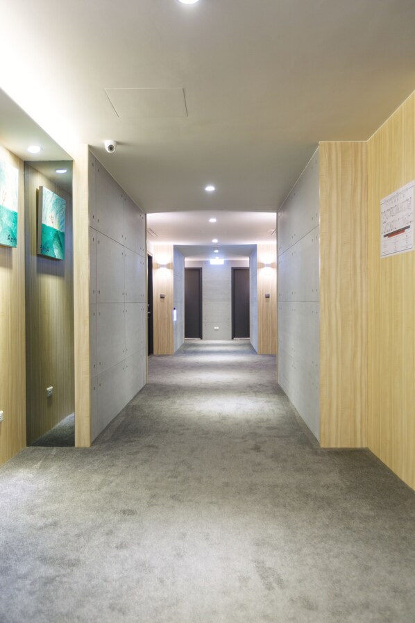 A corridor with lockers on both sides, a carpeted floor, and a wooden wall on the right. - Hub Hotel (Taoyuan City)