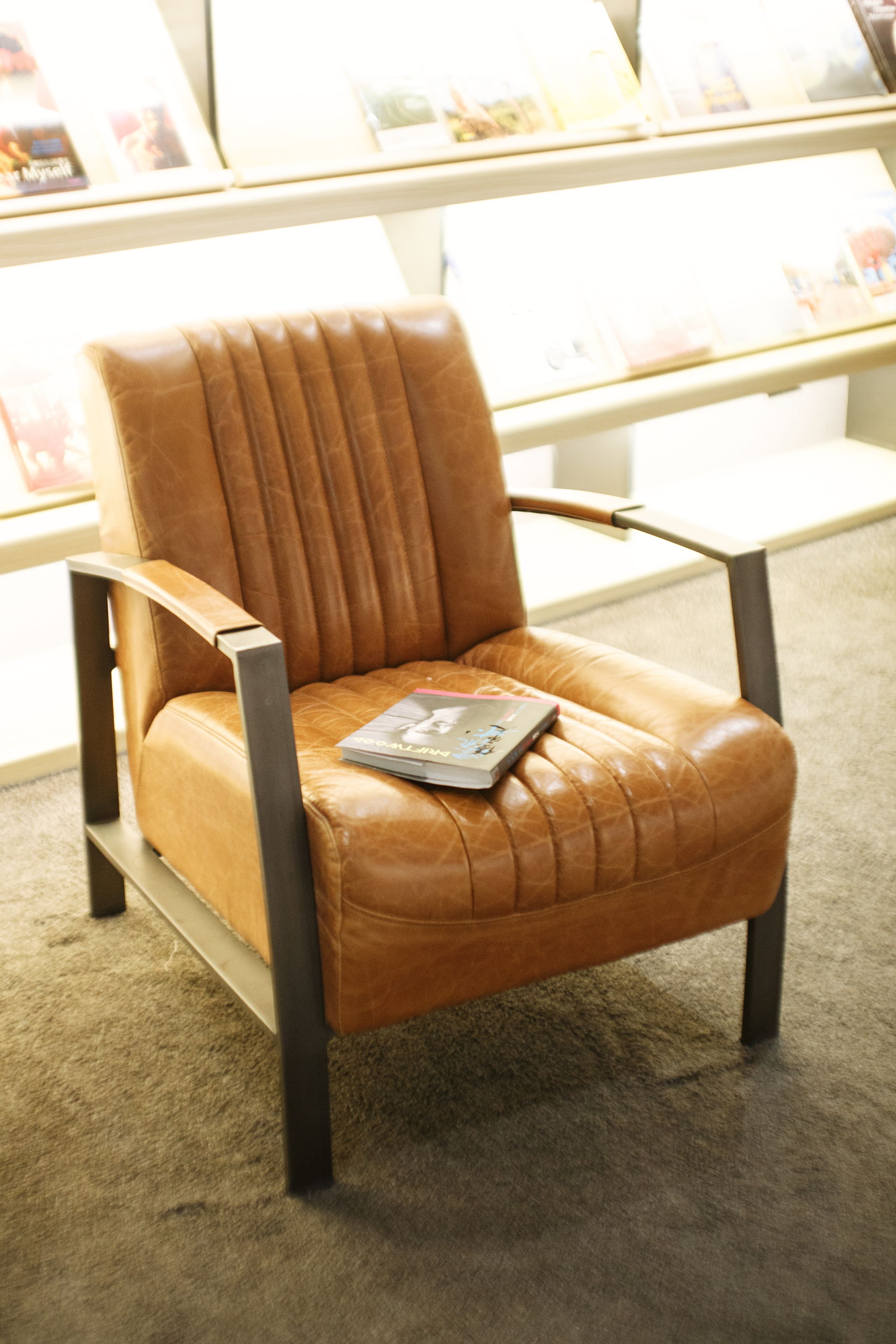 A brown leather chair with a magazine on it, positioned in front of a window with framed pictures.