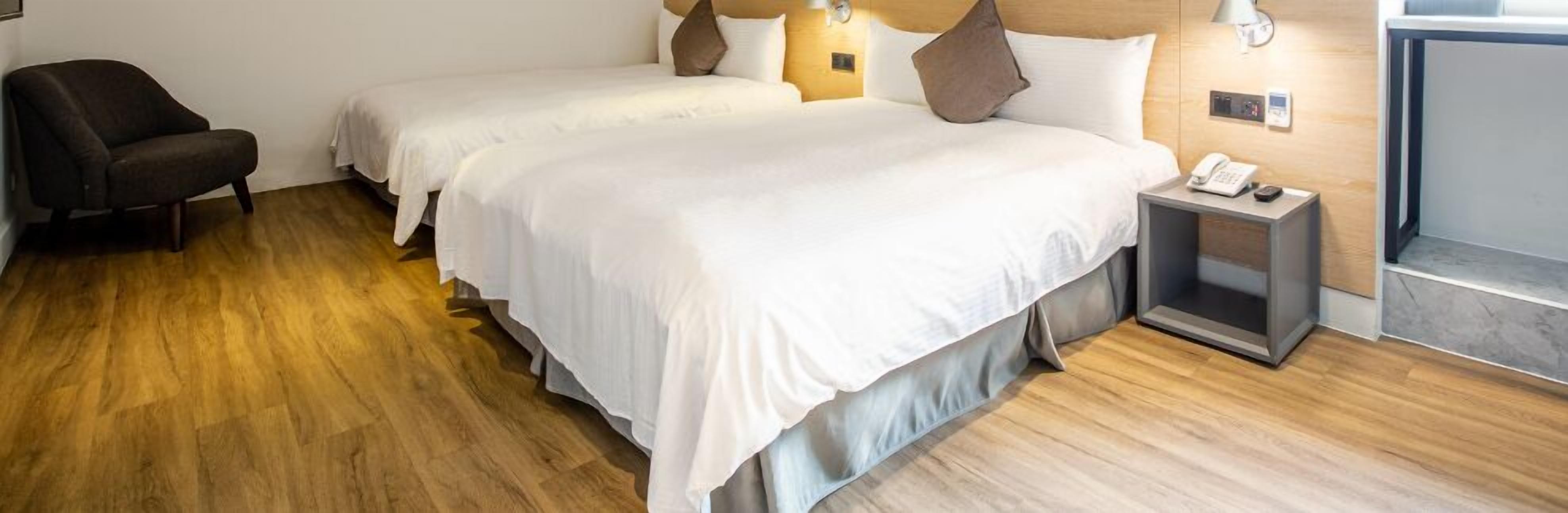 Hotelkamer met twee bedden, een stoel, een nachtkastje met telefoon en een wandlamp.