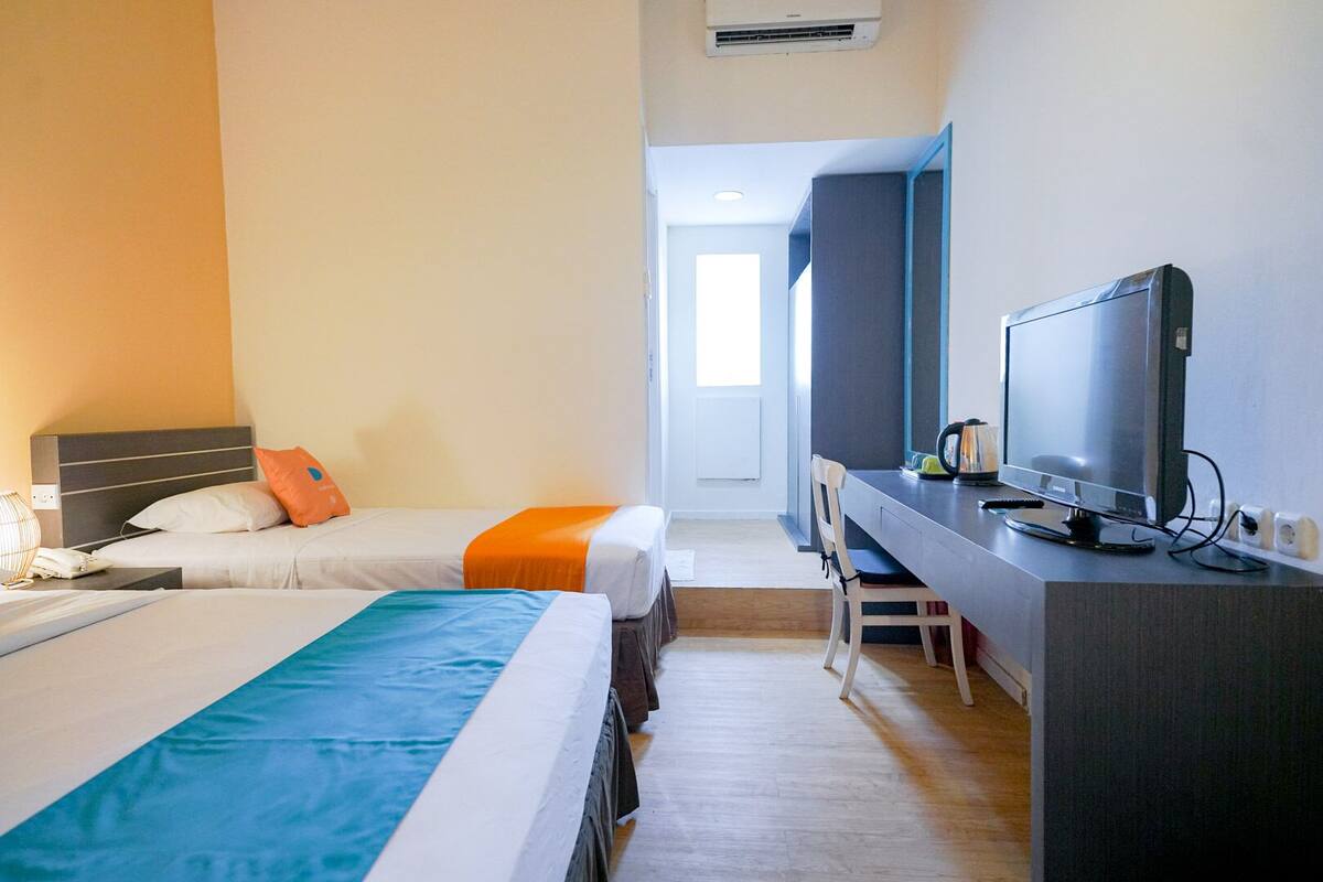 A hotel room with two beds, a desk with a TV, and a window.