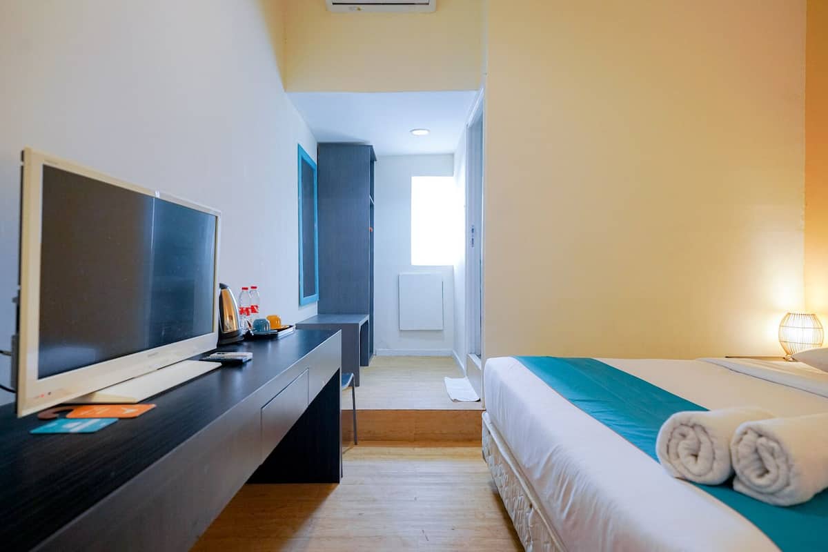 A hotel room with a bed, a desk with a TV, a bedside lamp, and a view of the hallway.
