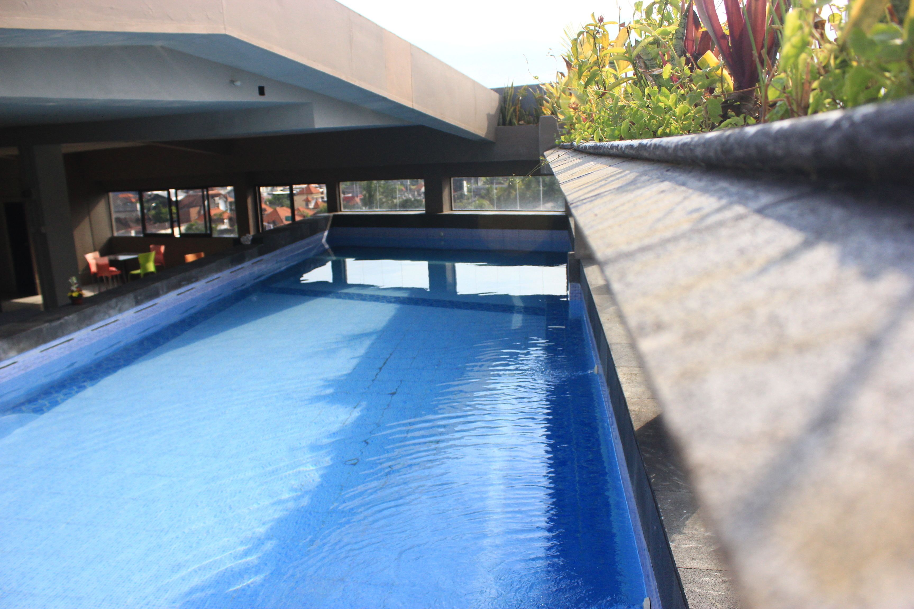 A swimming pool with a blue surface, surrounded by a concrete deck and a low wall.