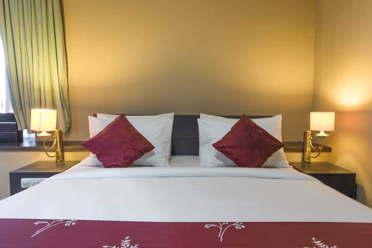A hotel room with a large bed, two nightstands, two lamps, and a window with curtains.