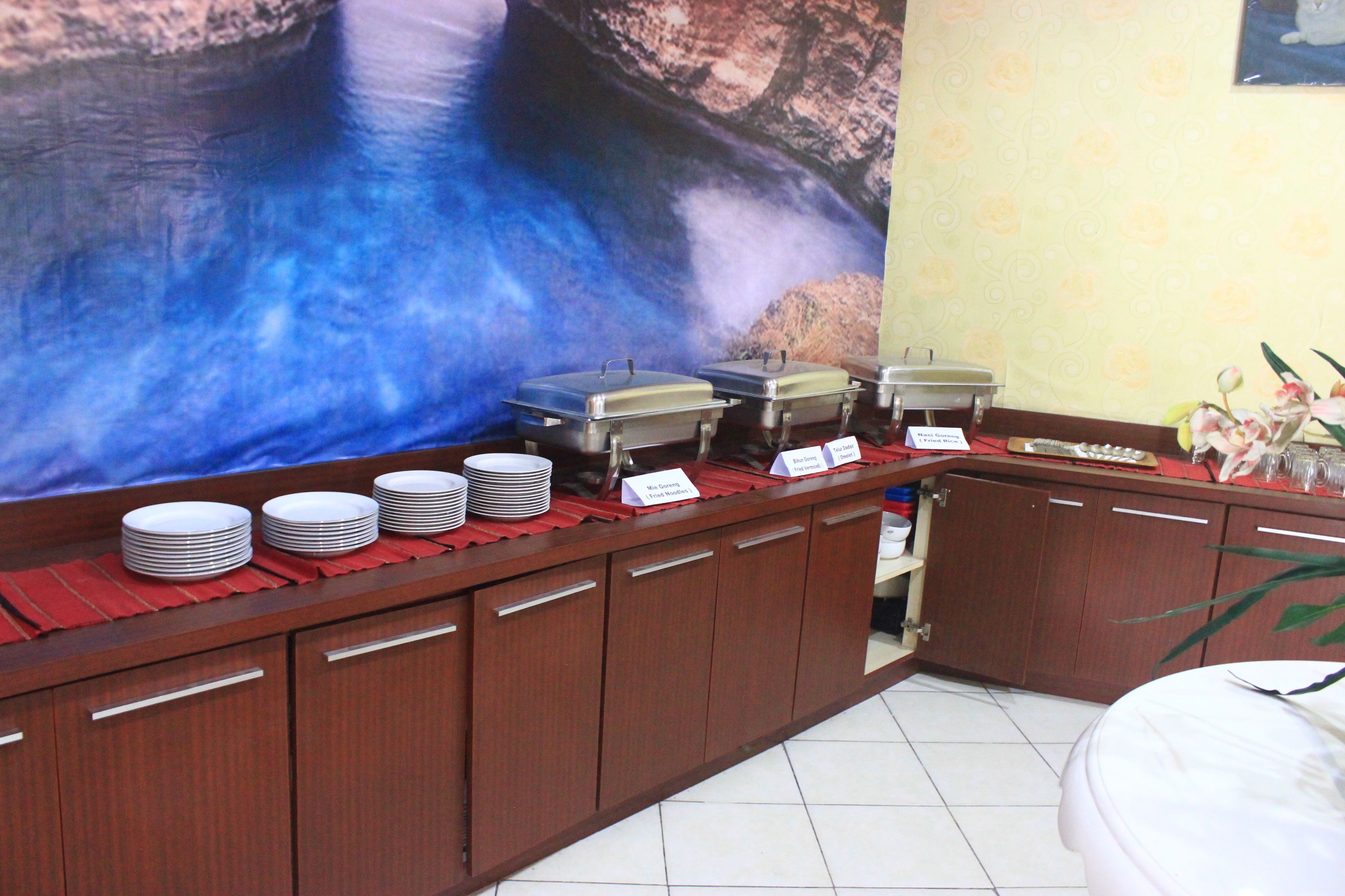 A buffet setup with multiple serving stations, a large decorative wall, and a small plant on the right.