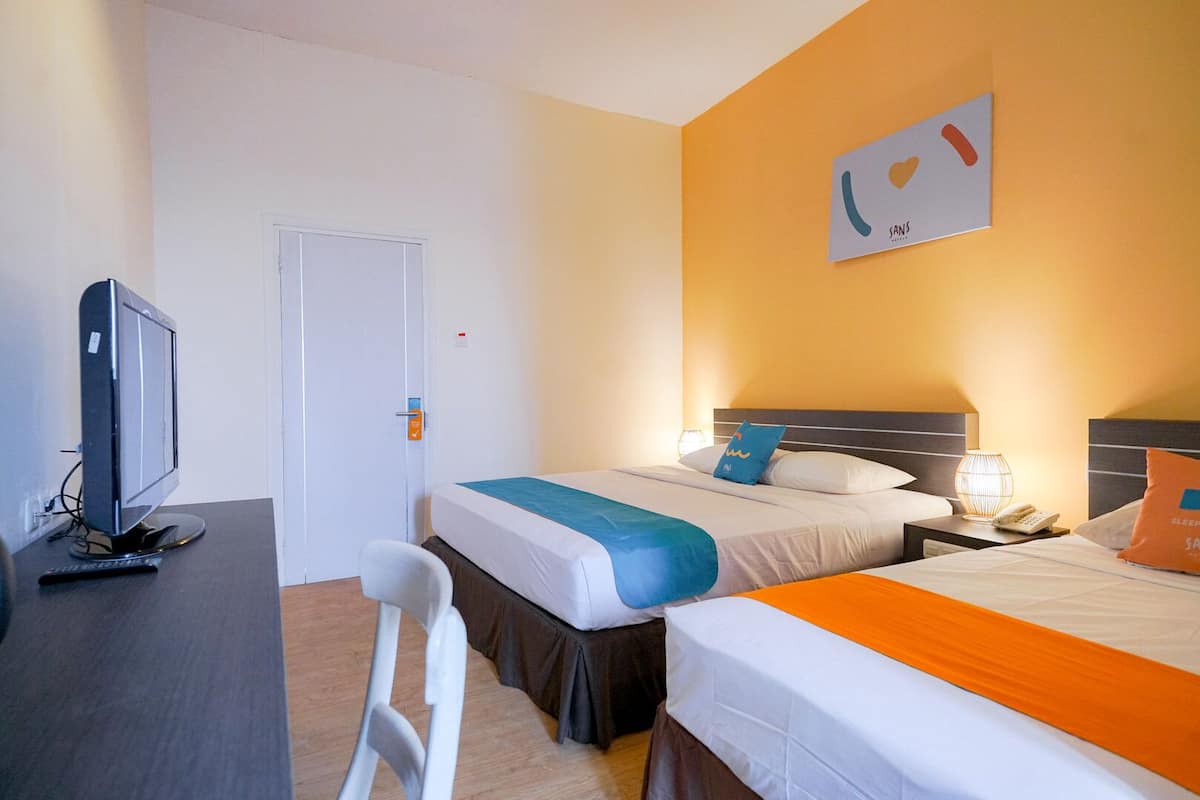 A hotel room with two beds, a desk with a computer, a chair, and a door.