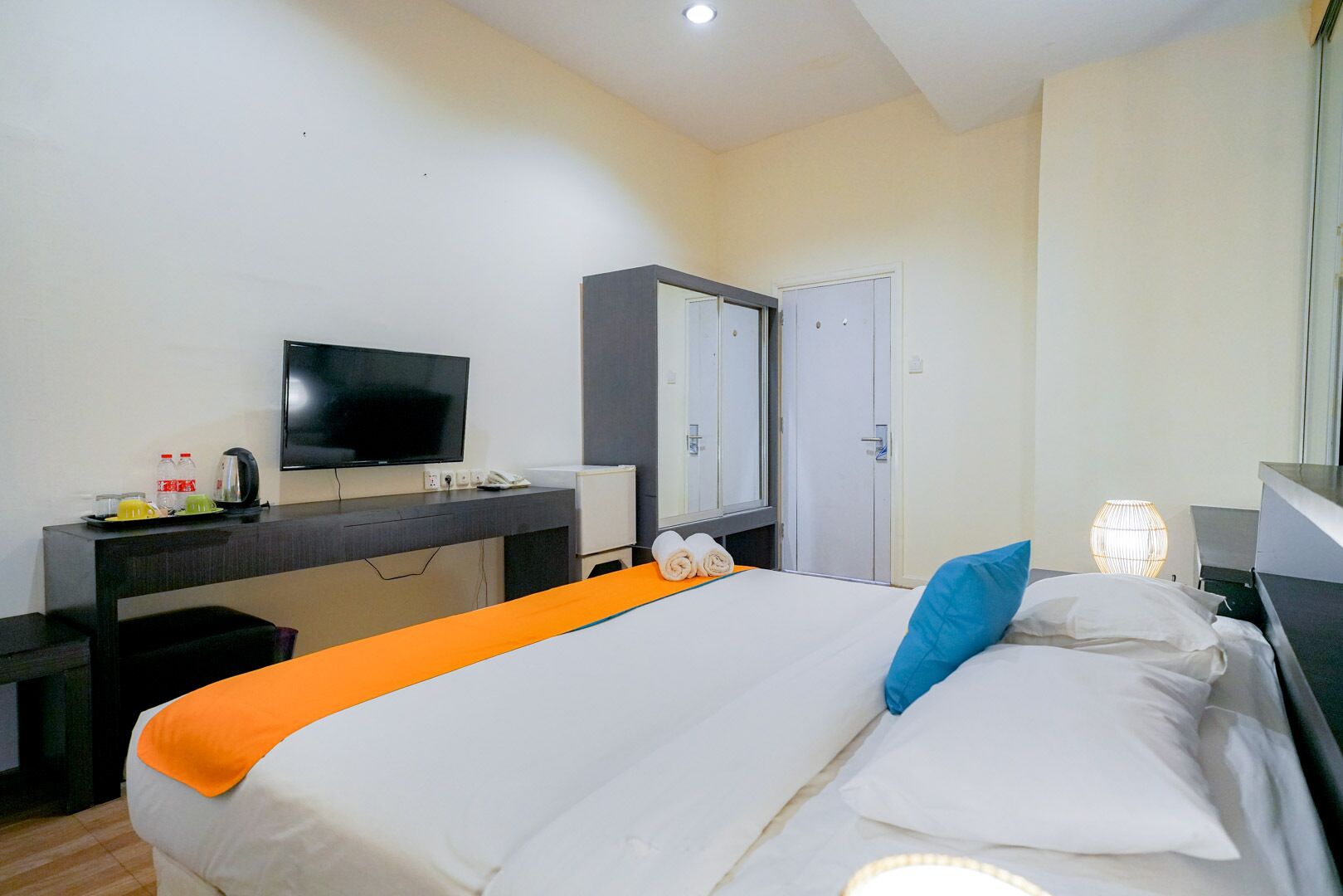A hotel room with a bed, a desk with a television, a mirror, and a wardrobe.