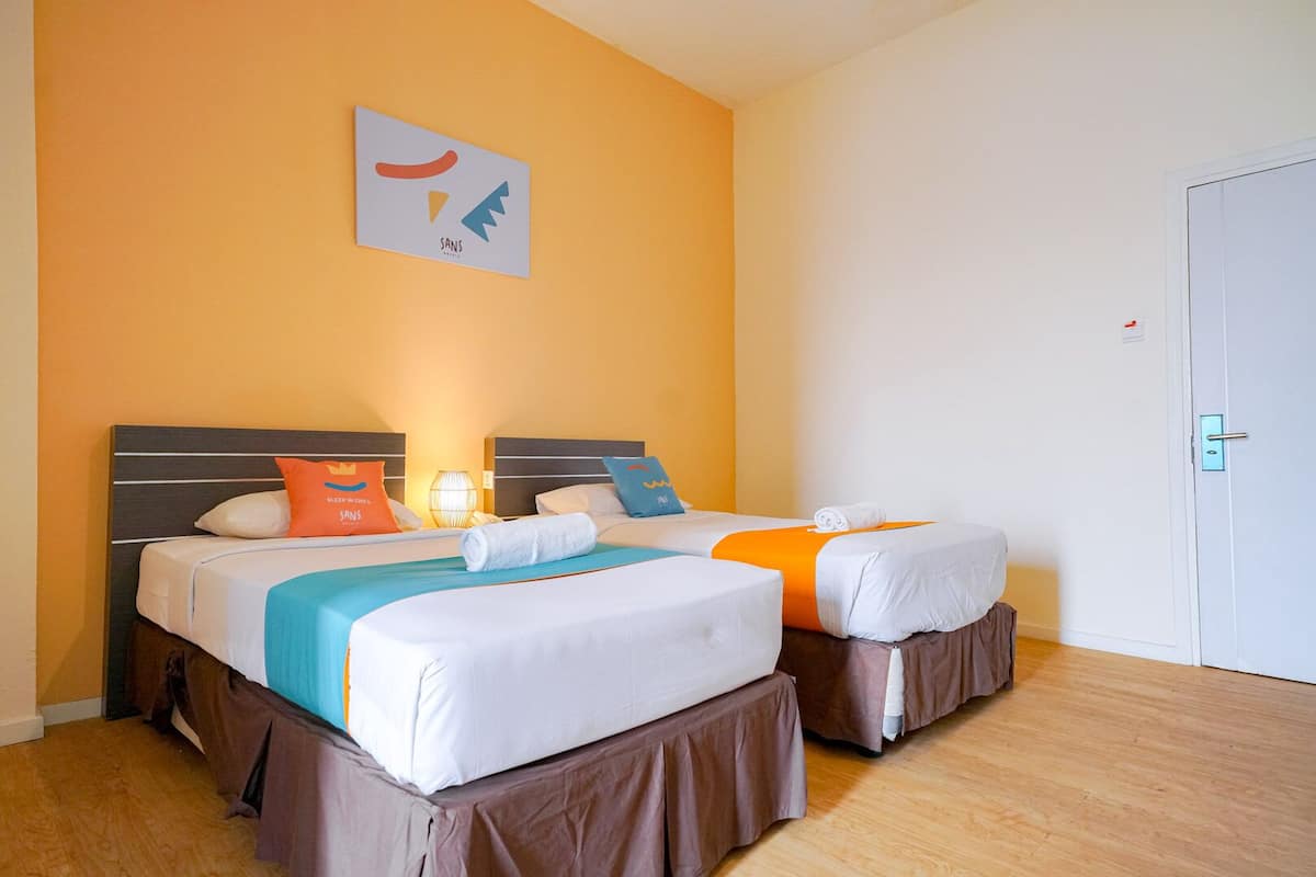 A hotel room with two beds, each with a headboard, white bedding, and decorative pillows. There is a wall-mounted artwork above the beds and a door to the right.