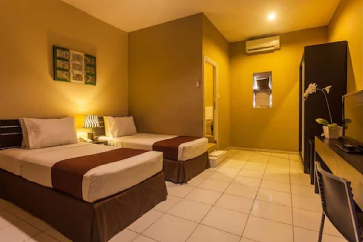 A hotel room with two beds, a desk, a chair, a small window, and an air conditioning unit.