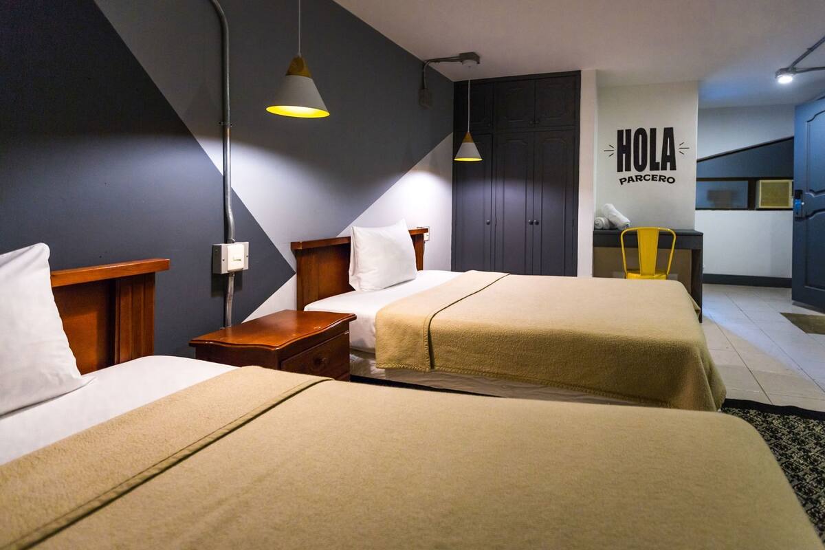 A hotel room with two beds, a desk, a chair, a wardrobe, and a kitchenette.