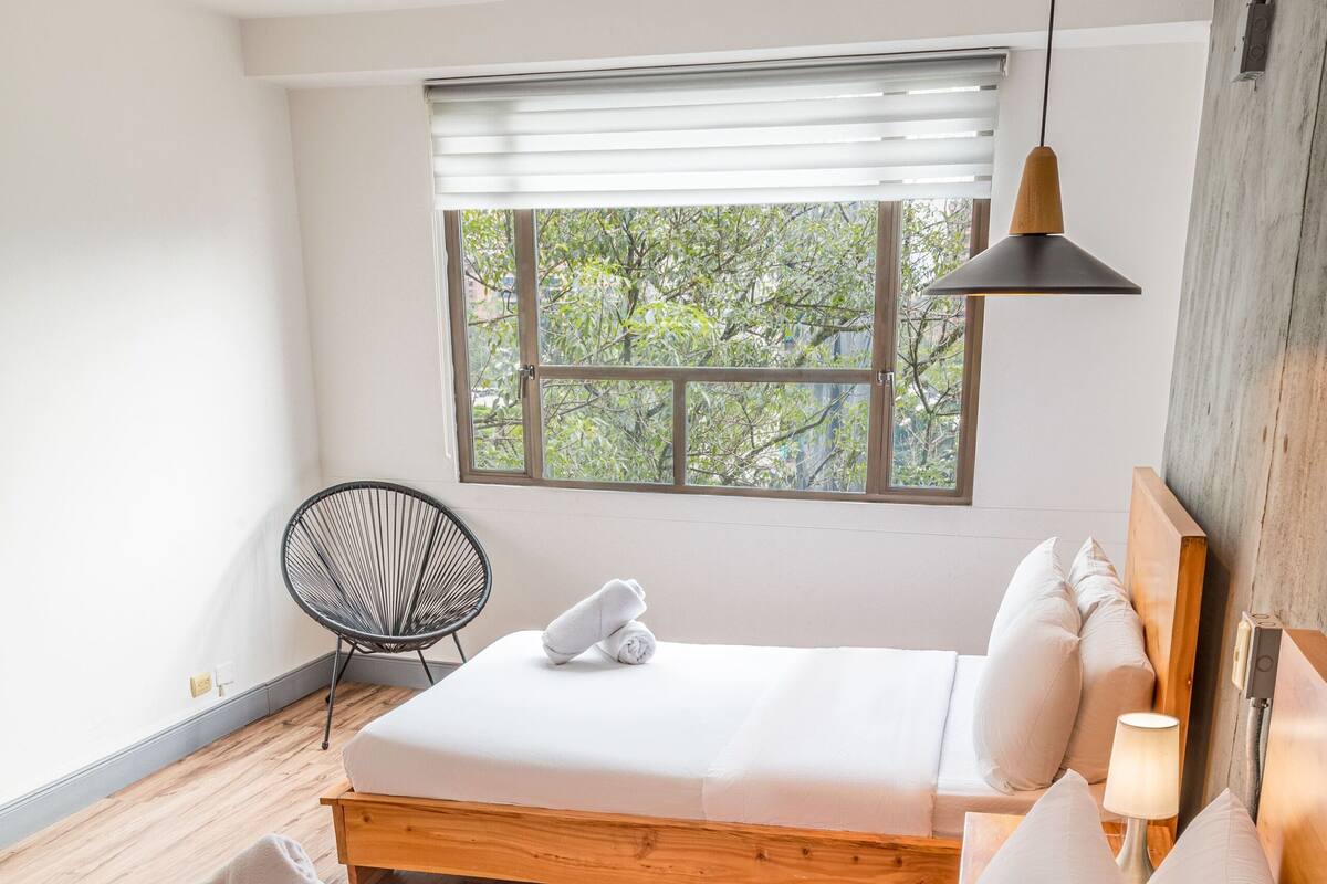 A bedroom with a large bed, a chair, a window, and a lamp.