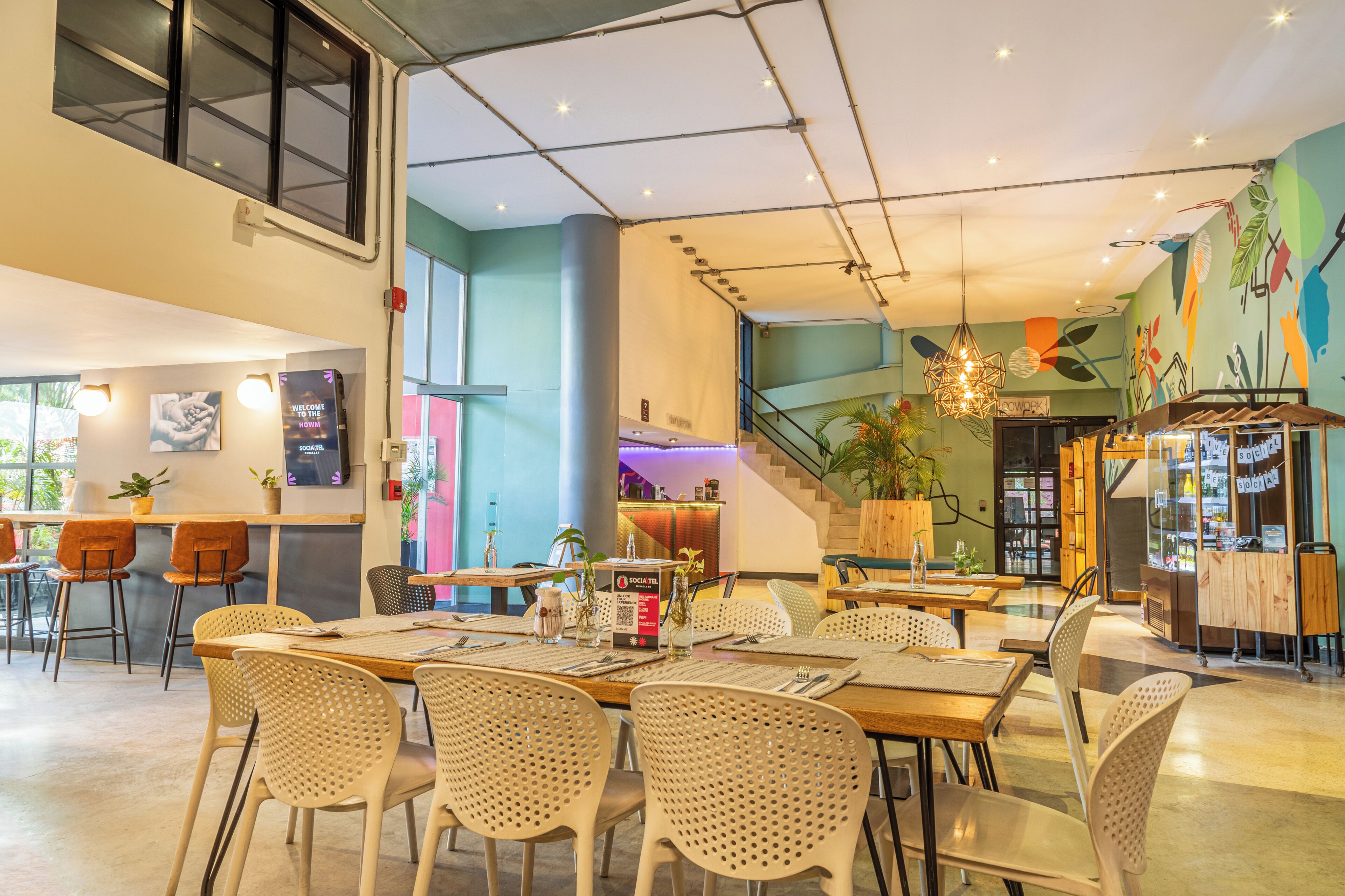 A modern restaurant with high tables, chairs, a staircase, and a colorful mural.