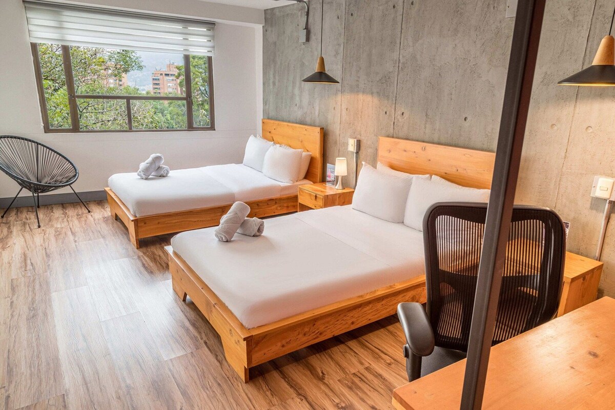 Habitación de hotel con dos camas, suelo de madera, una silla y un escritorio.