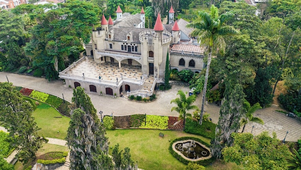 Ein großes, schlossartiges Gebäude mit mehreren Türmen, umgeben von üppiger Vegetation und einem gepflegten Garten.