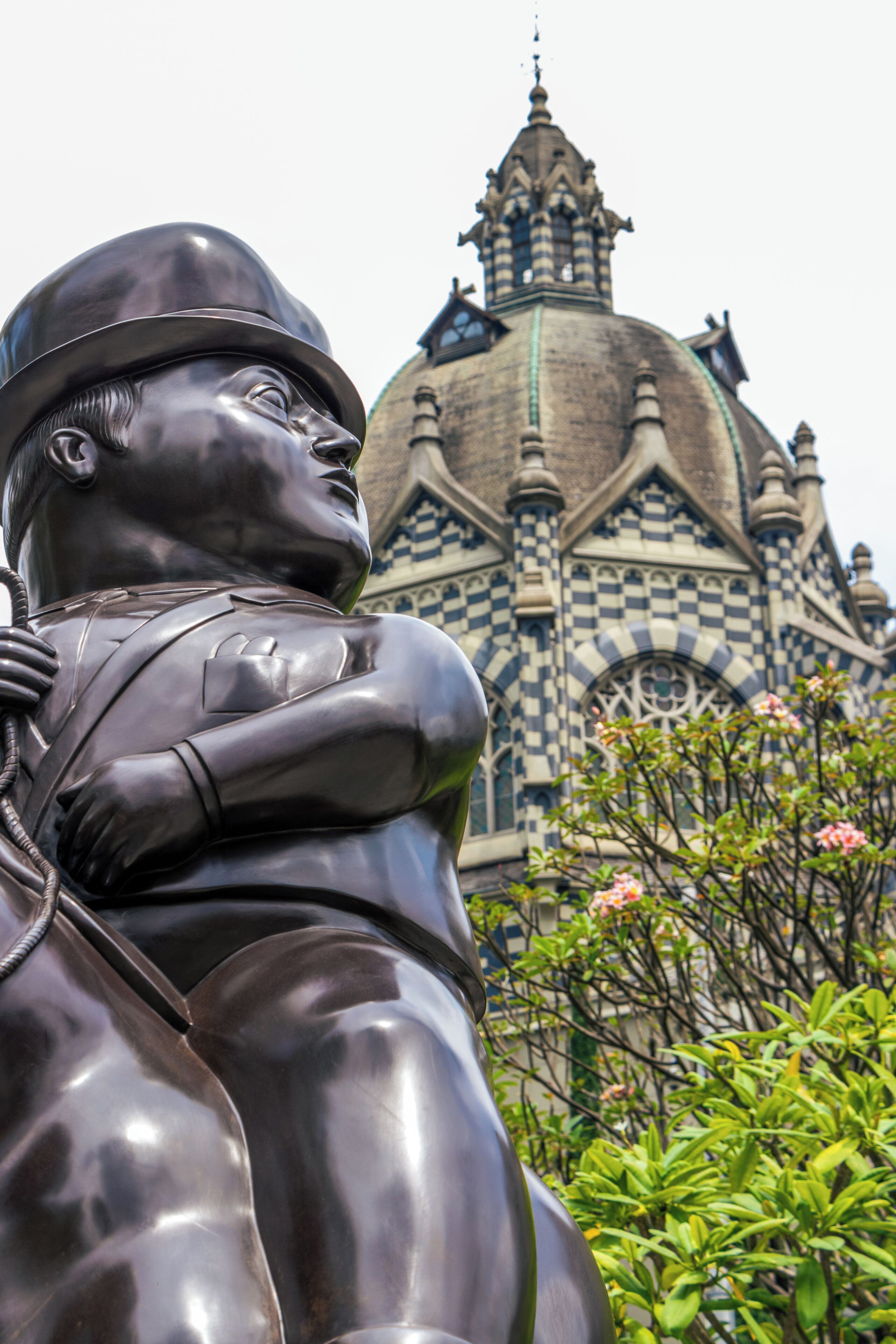 Una estatua de un hombre con casco y un niño, con un edificio de fachada a cuadros en el fondo.