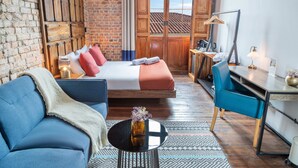 A modern hotel room with a brick wall, a bed with red and white bedding, a blue sofa, a small round table with a vase, and a desk with a lamp. - Delgadillo Boutique Hotel by Socialtel (Bogotá)