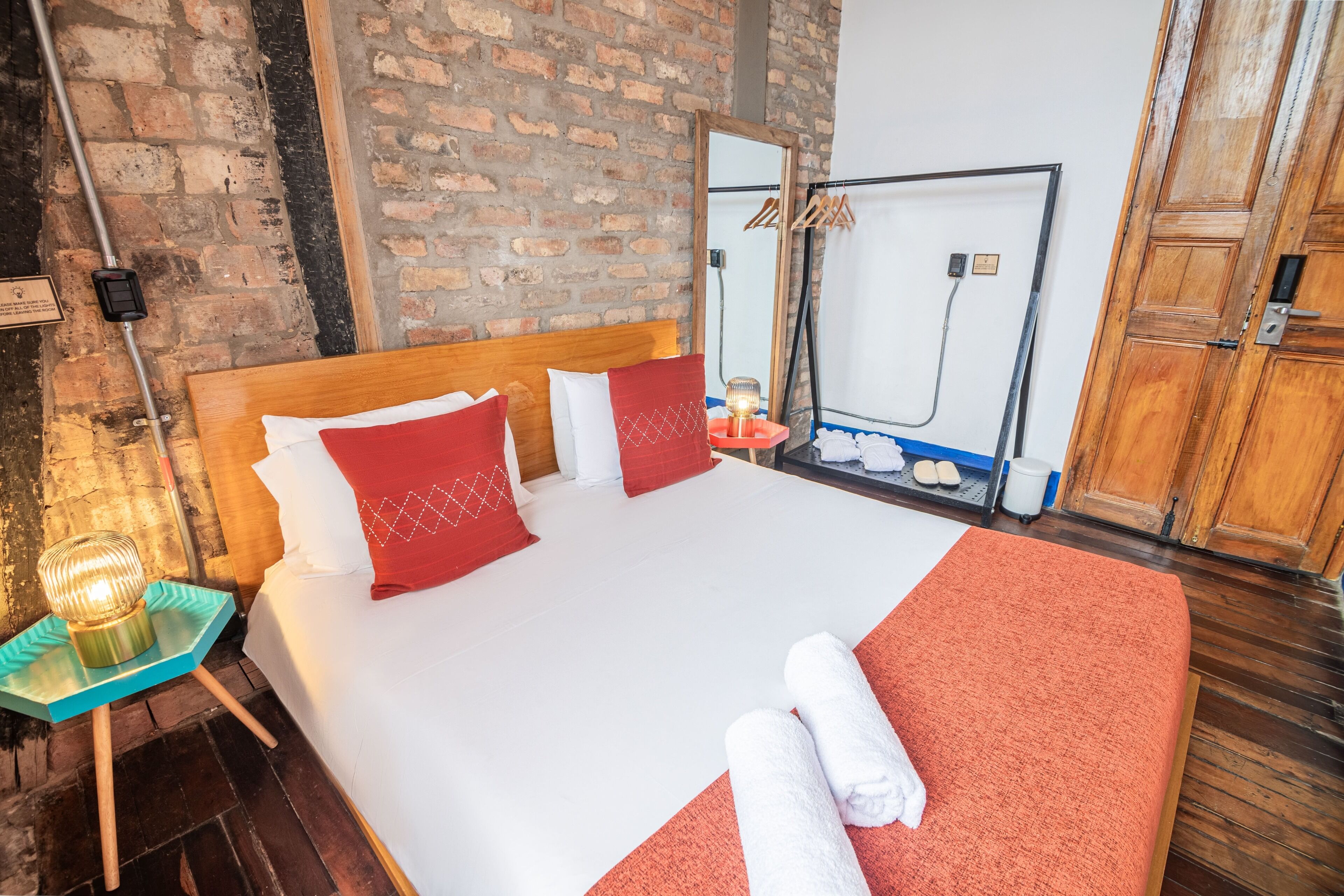 Ein Hotelzimmer mit einem großen Bett, rot-weiß gestreifter Bettwäsche, einem hölzernen Kopfteil, einem Nachttisch mit Lampe und einer Ziegelwand.