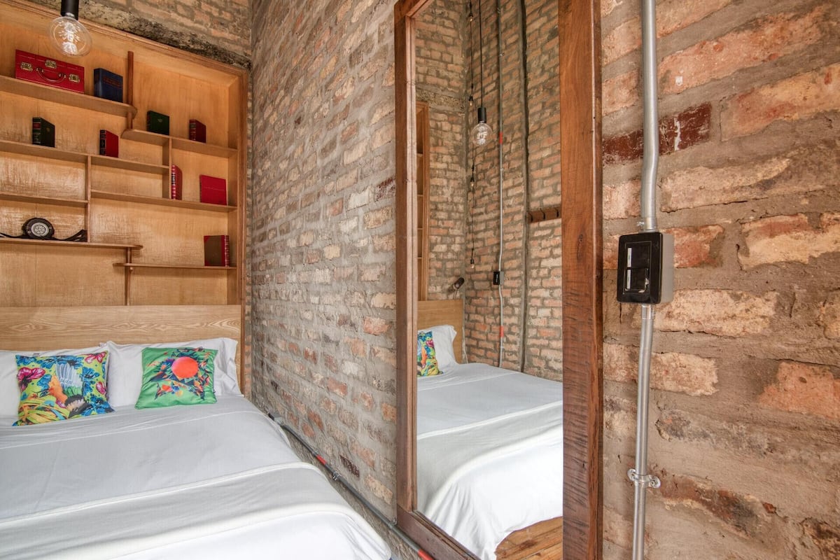 A room with two beds, a wooden bookshelf, and a brick wall.