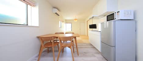 A compact kitchen with a dining area, featuring a refrigerator, microwave, and wooden table with chairs.
