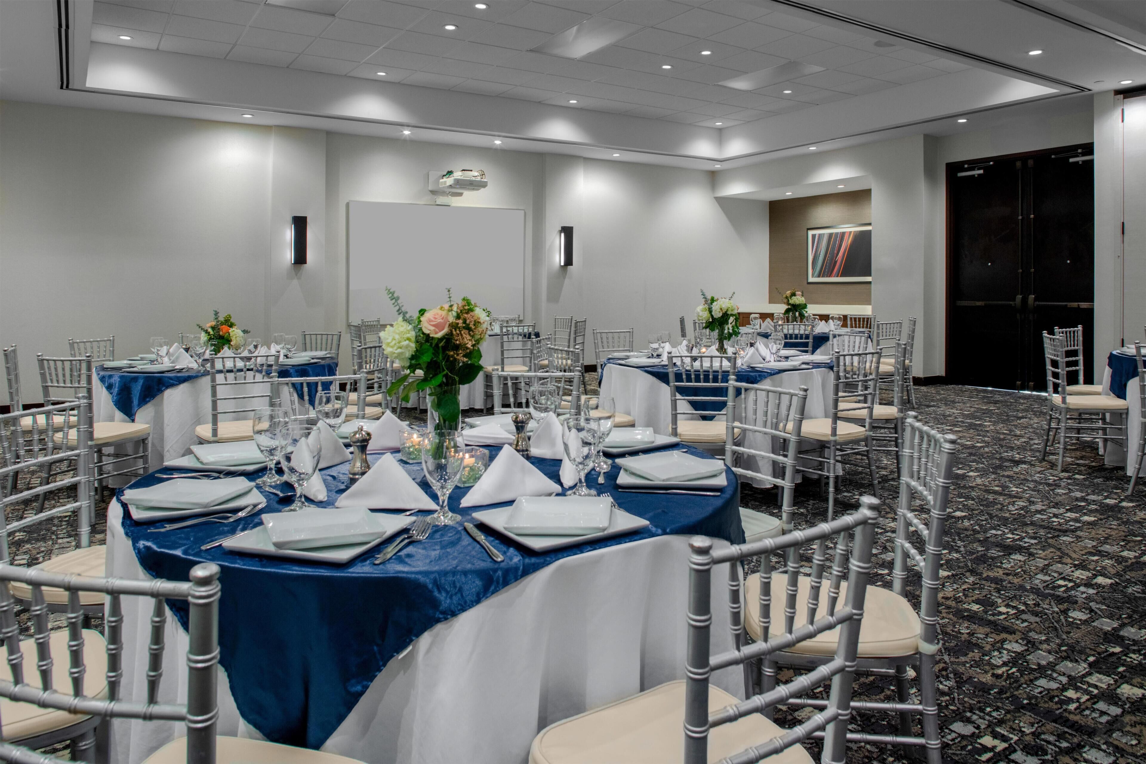 A conference room with round tables, white chairs, and blue tablecloths.