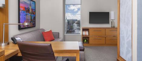 Een hotelkamer met een bureau, stoel, bank, televisie en een schilderij aan de muur.