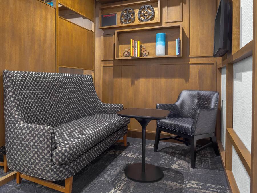 Une pièce avec un canapé à motifs, une petite table, une chaise et des étagères en bois ornées de livres et d’objets décoratifs.