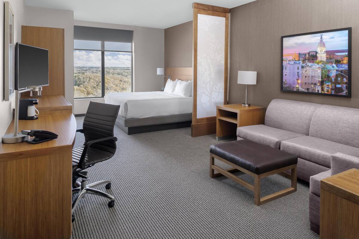 Una habitación de hotel con cama, escritorio, silla, sofá y un cuadro en la pared.