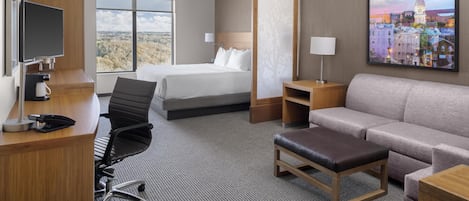 Ett hotellrum med en säng, ett skrivbord, en stol, en soffa och en tavla på väggen.