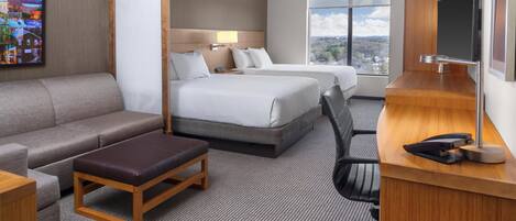 A hotel room with a sofa, two beds, a desk, and a TV.