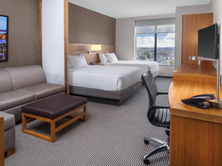 A hotel room with a sofa, two beds, a desk, and a TV.