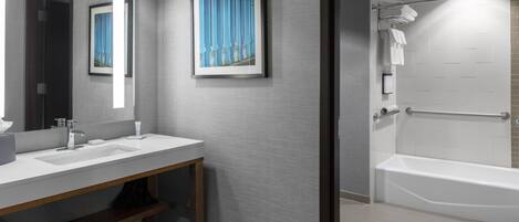 A modern bathroom with a sink, mirror, framed artwork, and a shower area.
