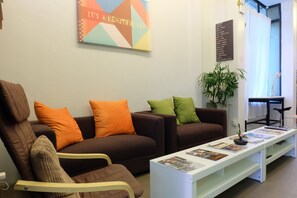 A modern living room with a brown sofa set, a white coffee table with magazines, and a colorful abstract painting on the wall. - DewyHouse (Chiang Mai)
