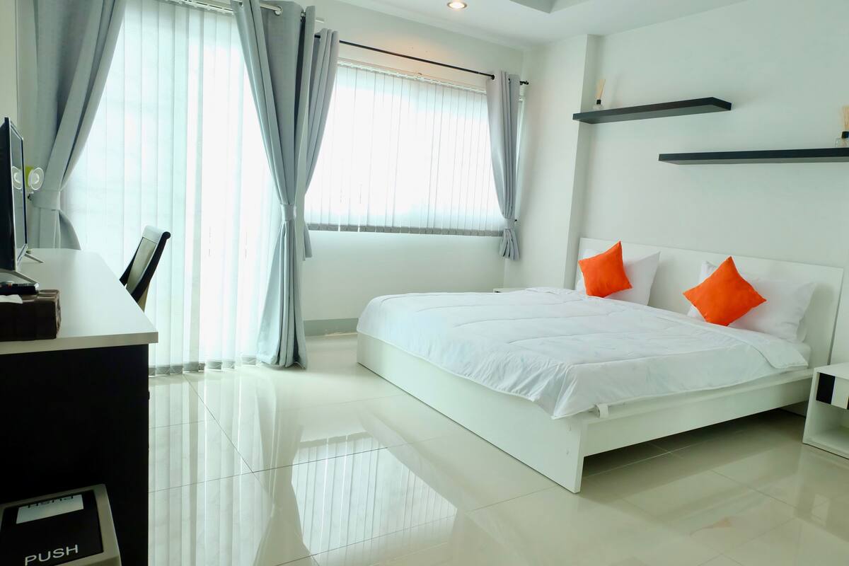 A modern hotel room with a large bed, a desk with a computer, and a window with curtains.