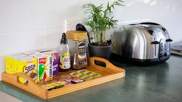 Una encimera de cocina con cajas de cereal, un tarro de miel, un frasco de especias, un tostador y una planta en maceta.