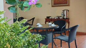 A dining area with a round table, black wicker chairs, and a painting on the wall.