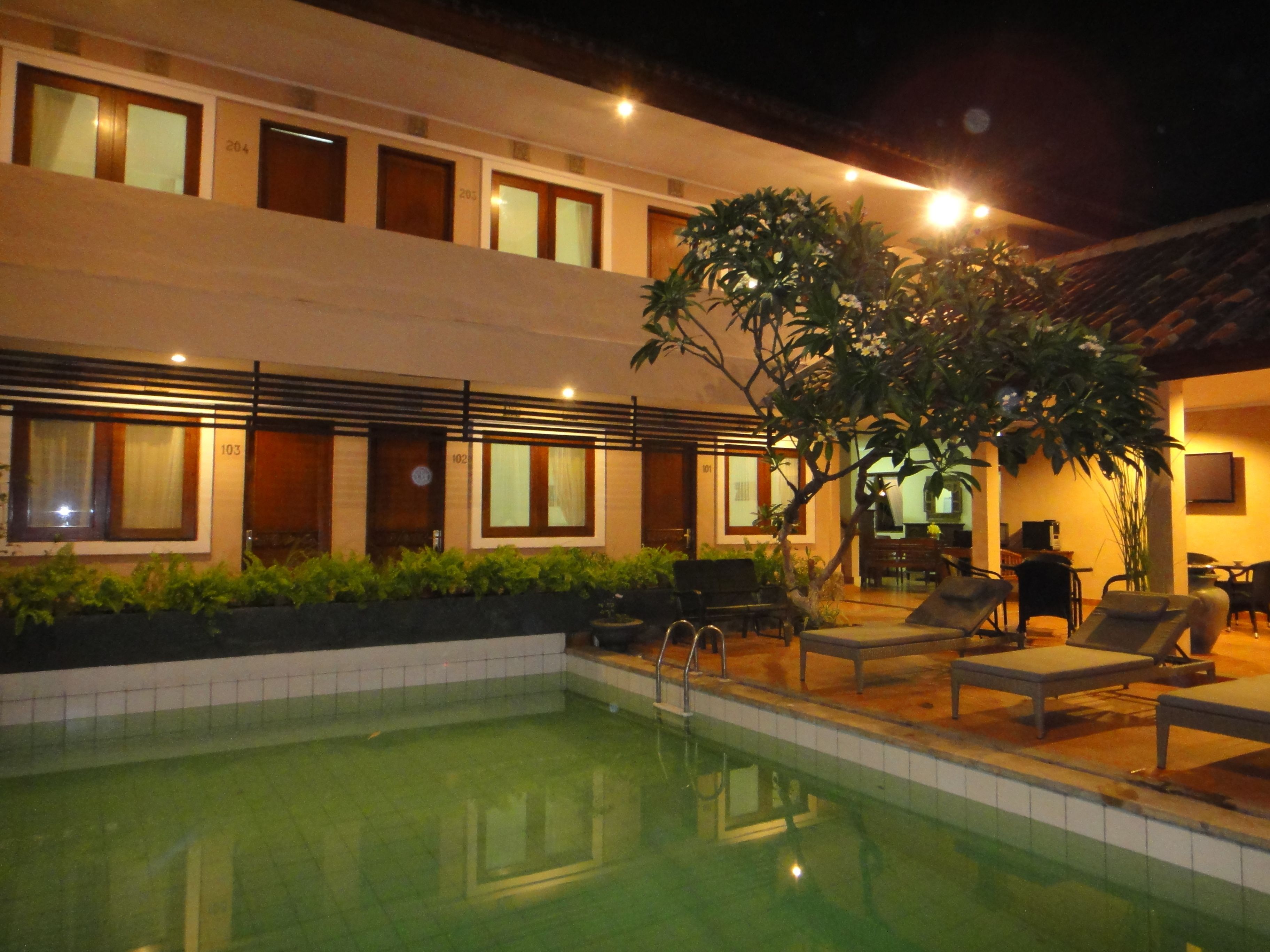 A hotel with a swimming pool, outdoor seating, and a well-lit facade.