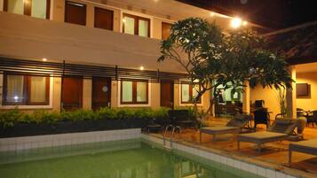 A hotel with a swimming pool, outdoor seating, and a well-lit facade.