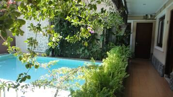 A pool area with a tiled floor, surrounded by lush greenery and a wooden pergola.