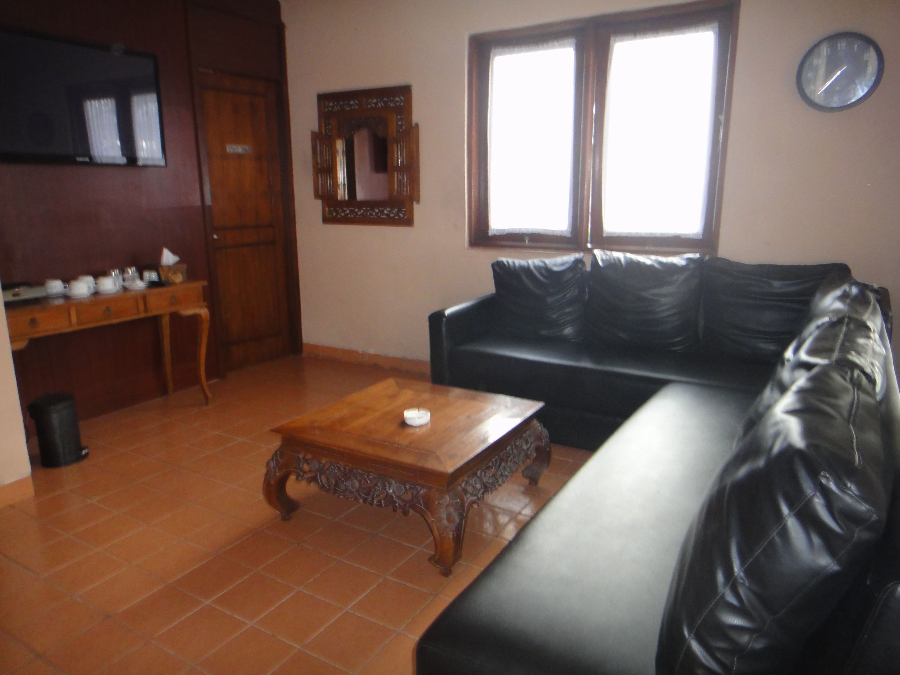 A living room with a black leather sofa, a wooden coffee table, a wooden cabinet, a mirror, and a clock on the wall.